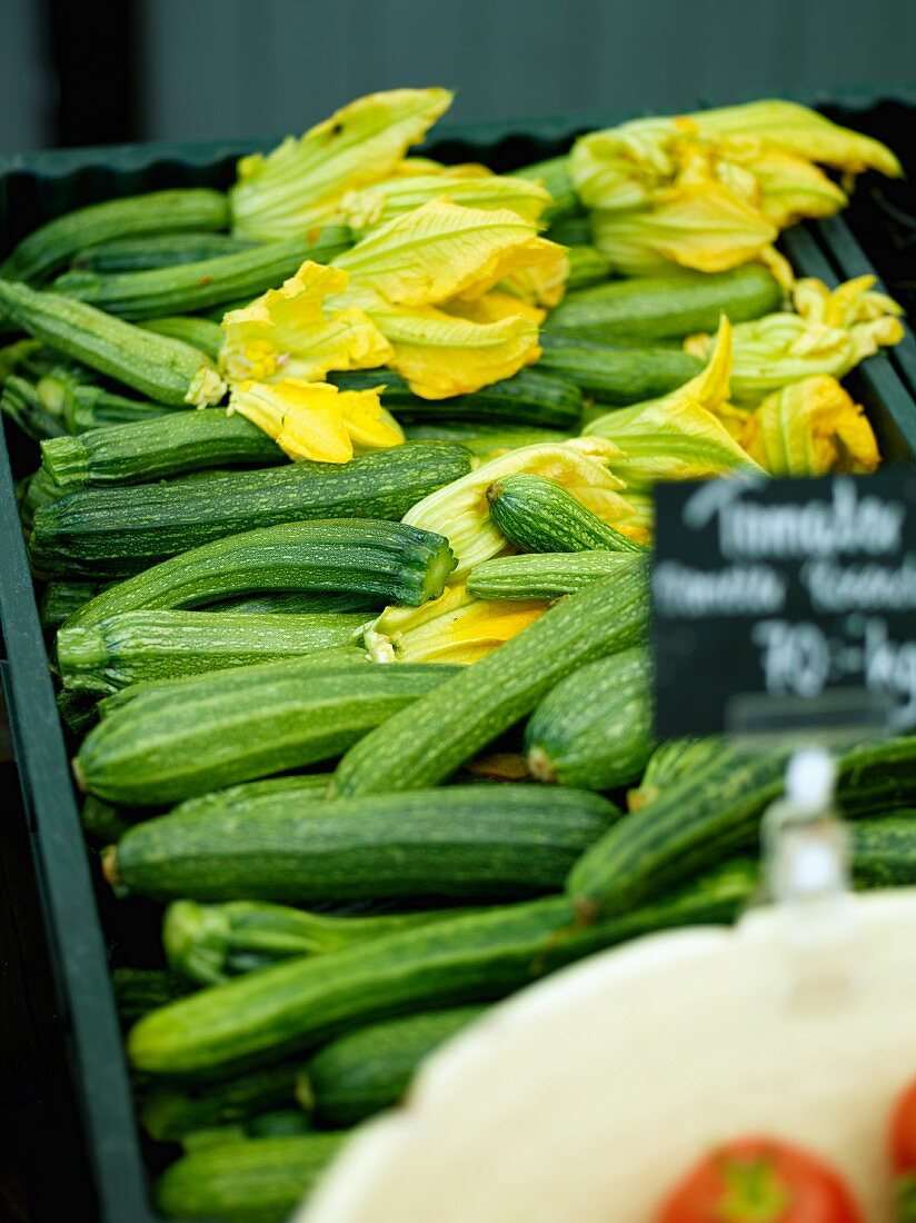 Fresh courgettes, some with flowers, in a crate on a market stall