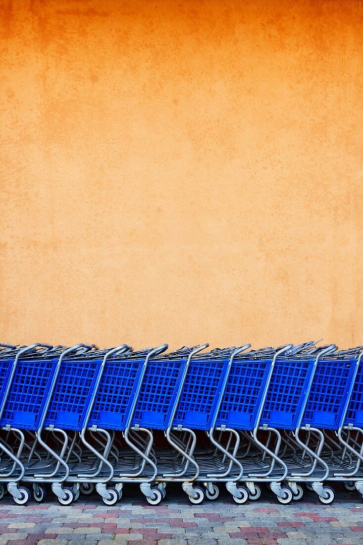 Blaue Einkaufswägen vor orangefarbener Hauswand