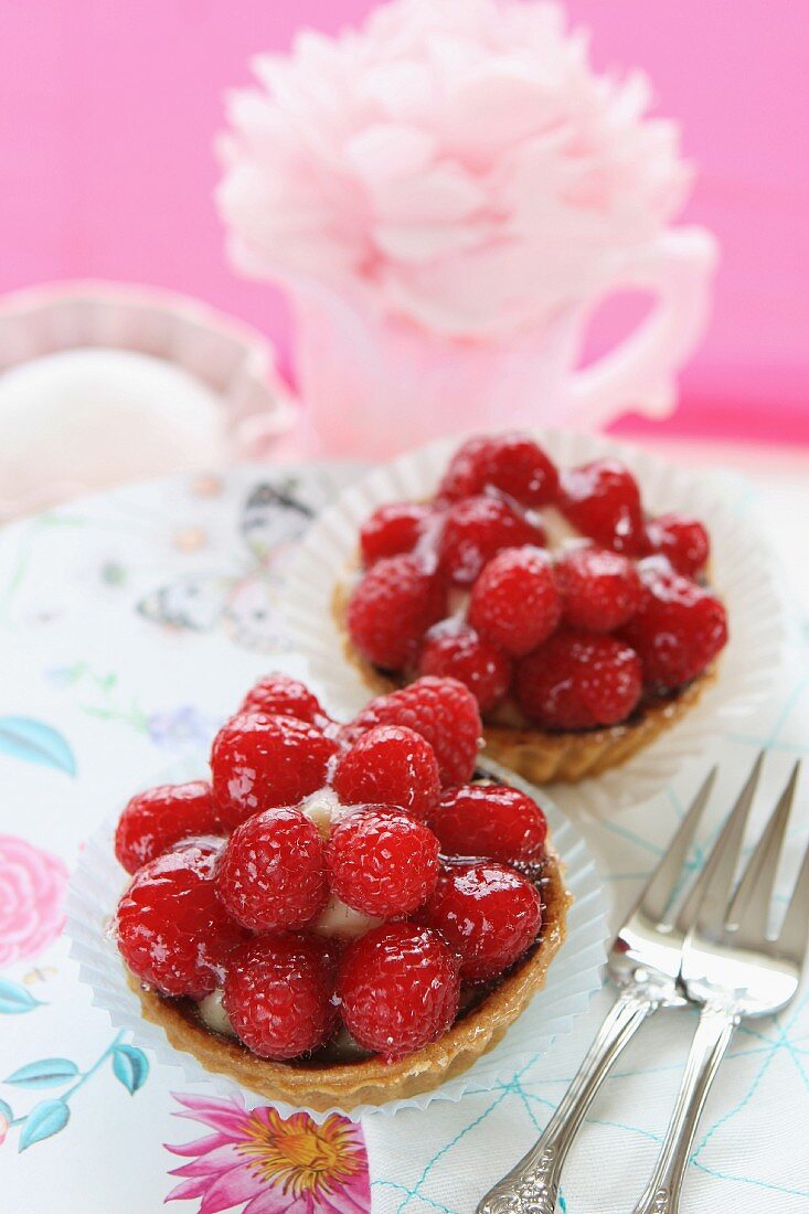 Two strawberry tartlets and cake forks on a floral tablecloth