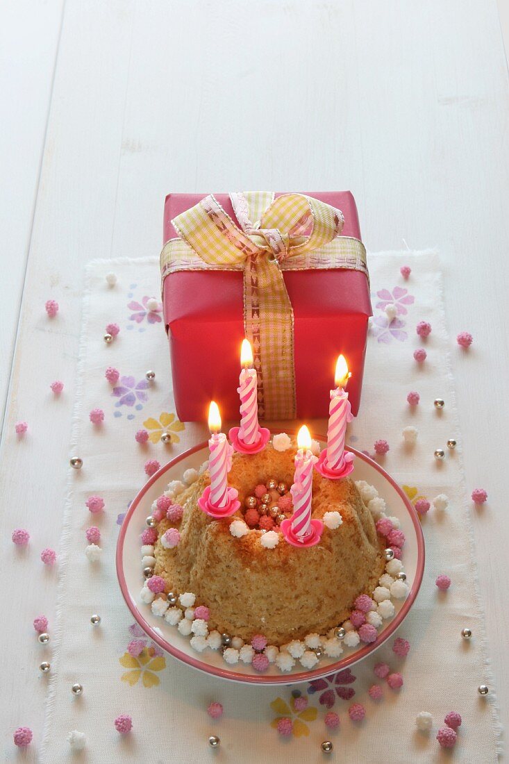 A birthday cake with four burning candles and a gift-wrapped present with a bow