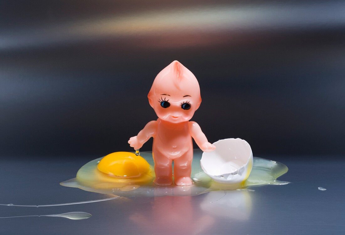 Winzige Babypuppe in rohem Ei stehend