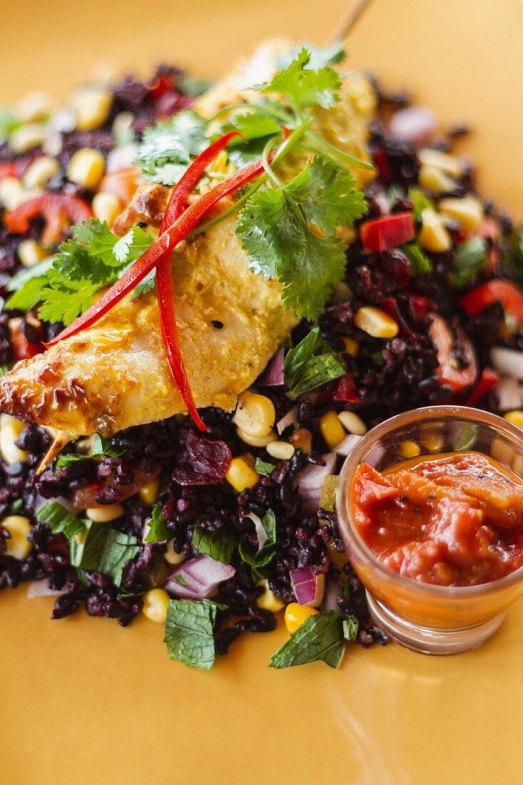 Chicken skewer with coriander leaves on black rice salad