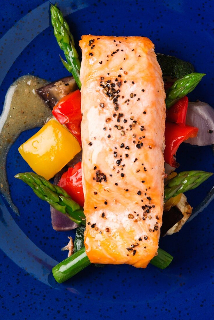 A salmon fillet on a bed of asparagus and peppers