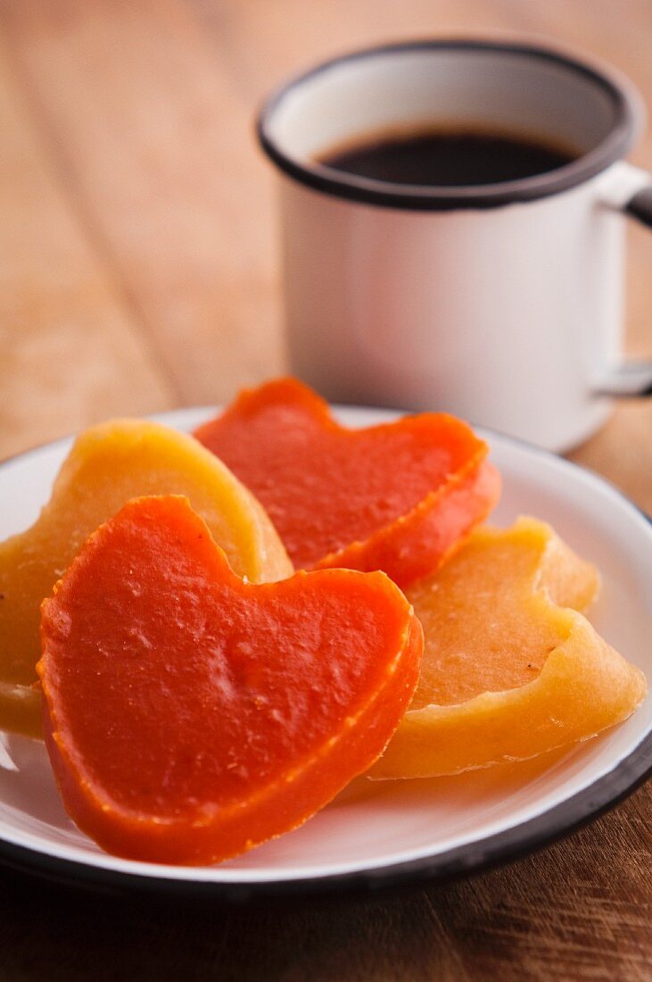 Heart-shaped candies of pumpkin (orange) and sweet potato (yellow) with cup of coffee on the background