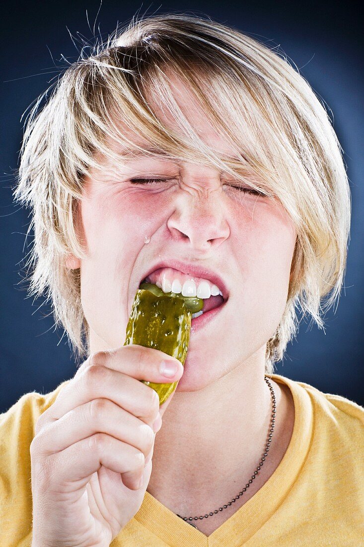 A young man biting into a gherkin