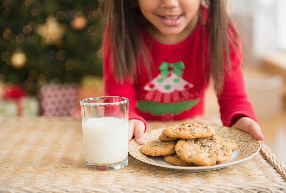 Mädchen stellt Cookies & Glas Milch auf Tisch für Santa Claus