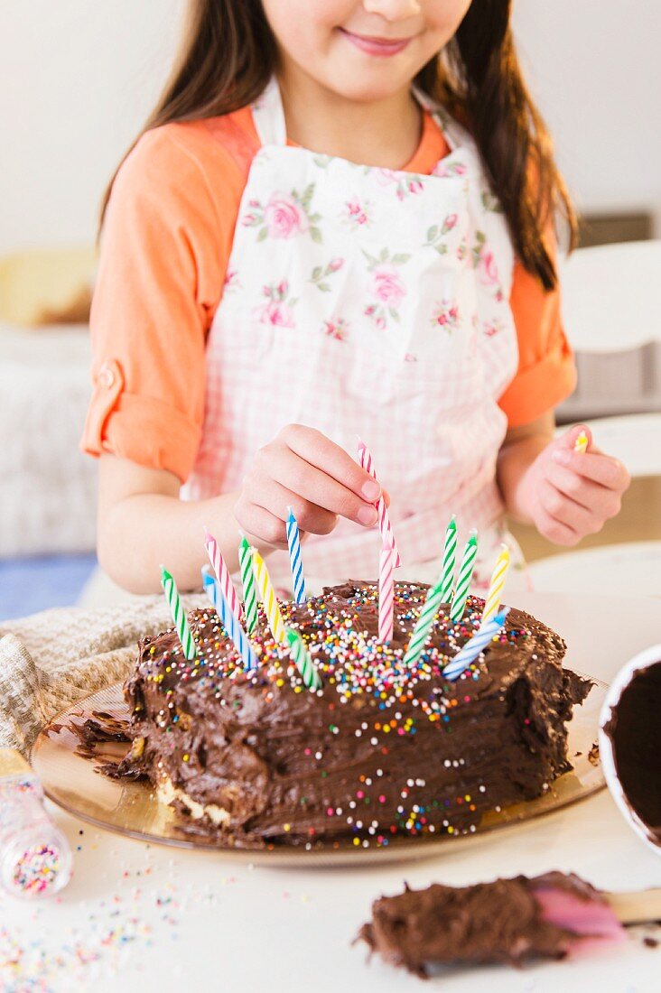 Mädchen dekoriert Schokoladentorte mit Geburtstagskerzen