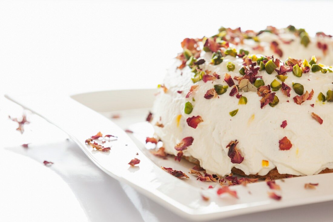 A Bundt cake with white icing, pistachios and rose petals