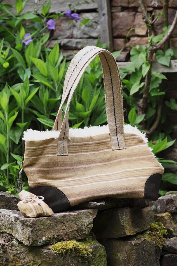 Hand-sewn handbag with fleecy lining on stone wall in garden