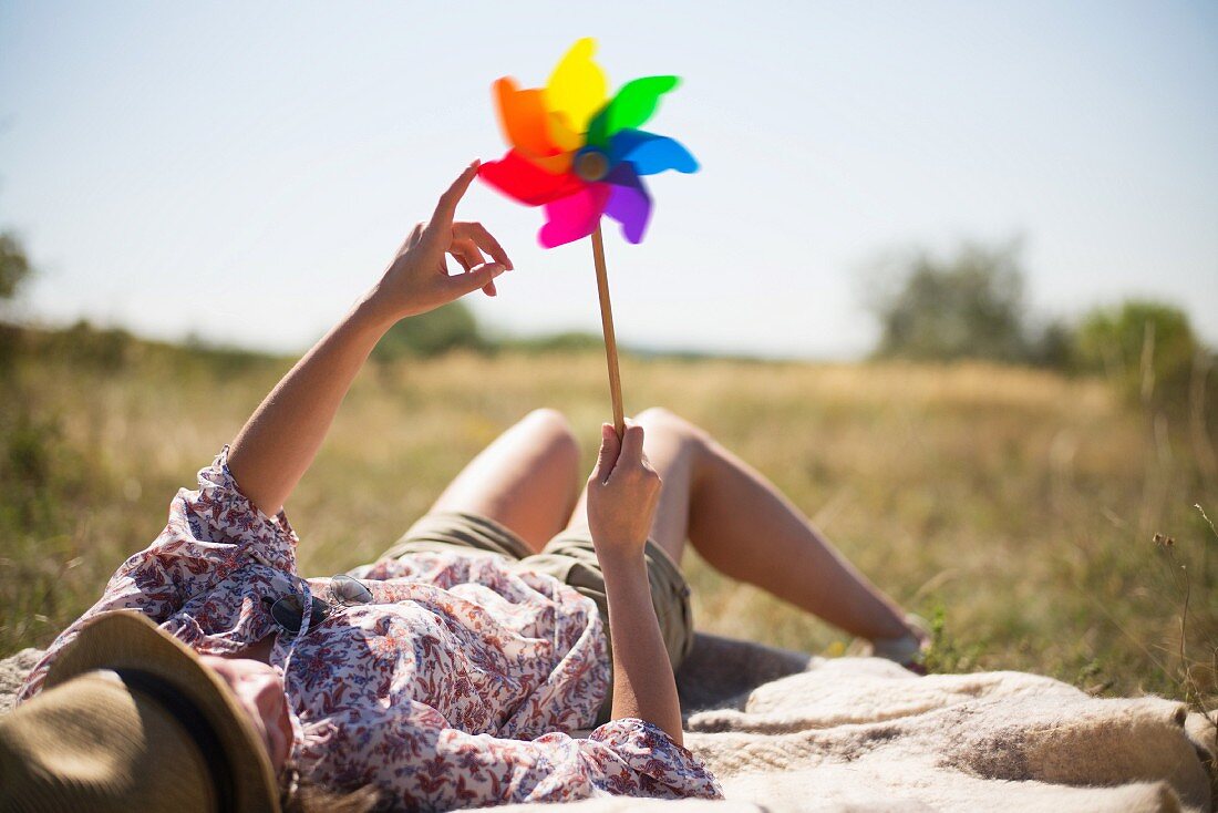 Frau auf Decke liegend mit buntem Windrad in der Hand