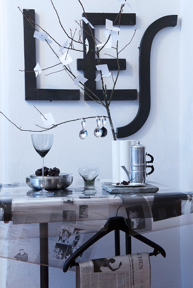 Schwarz-weiße Tischdeko mit Zeitungspapier, Zweig mit Zettelblättern und an die Wand gehängten Buchstabenformen