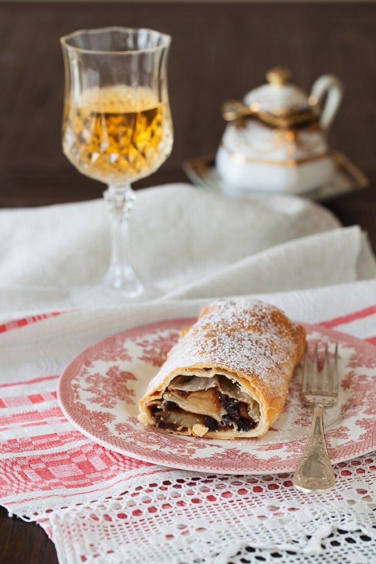 Apfelstrudel auf Teller vor einem Glas Wein