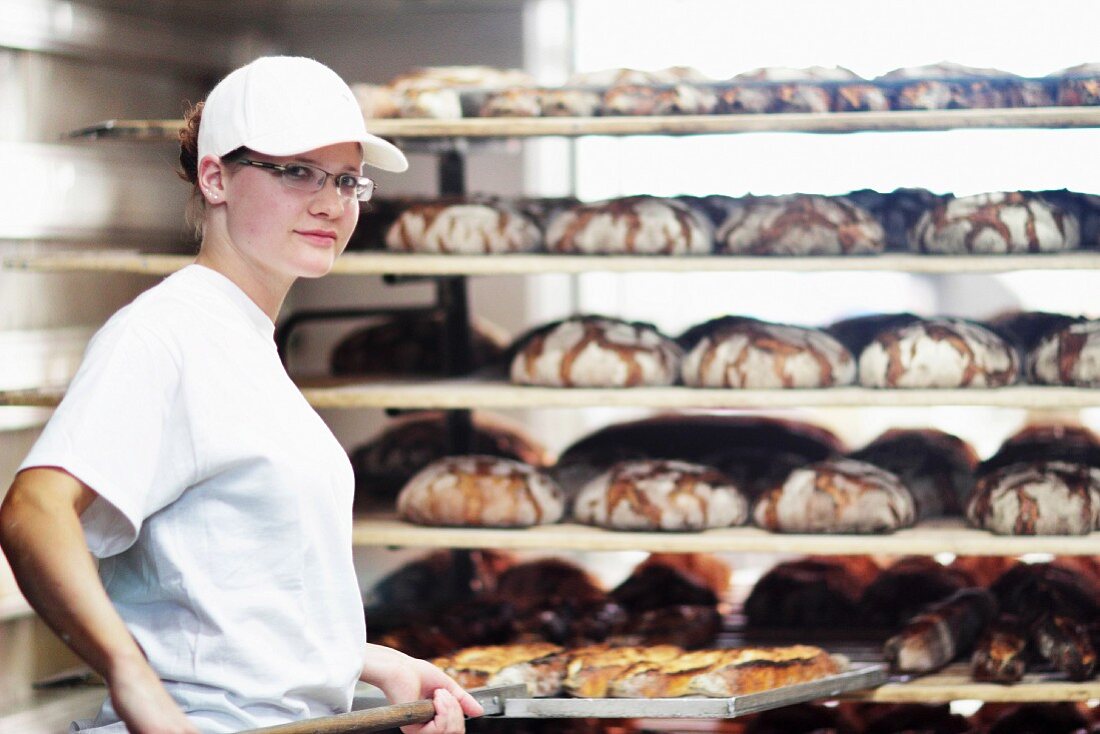 A young baker pushing a tray of freshly baked loaves onto a shelf