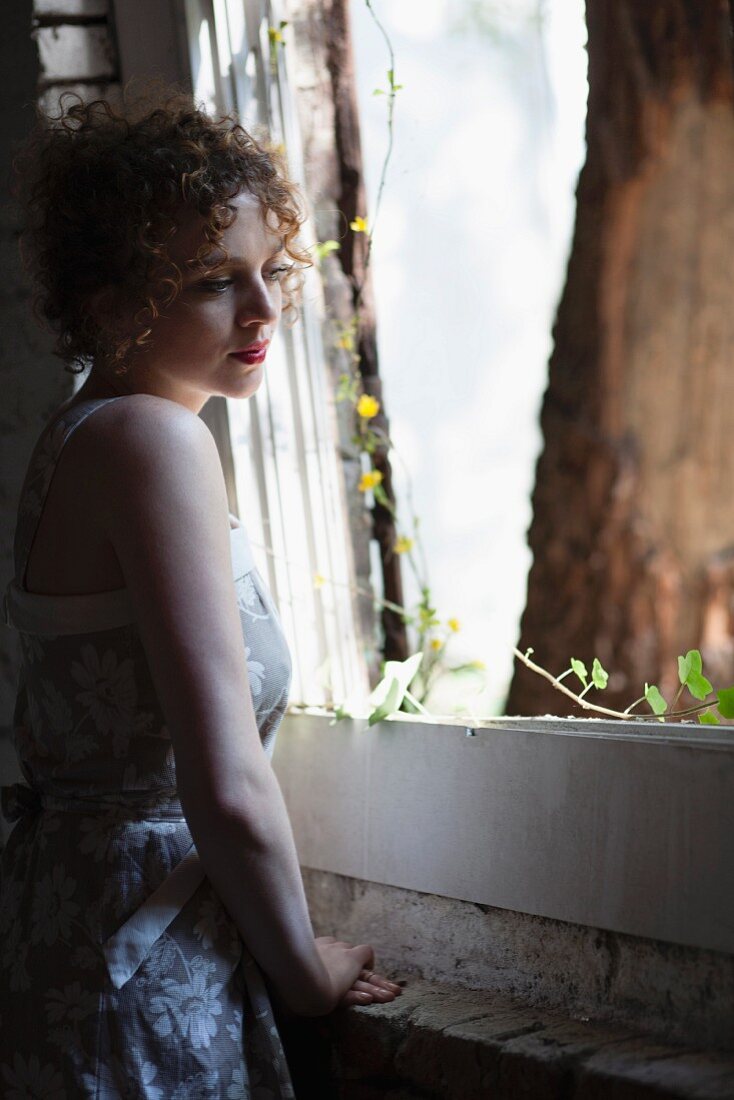 Young woman standing by window daydreaming