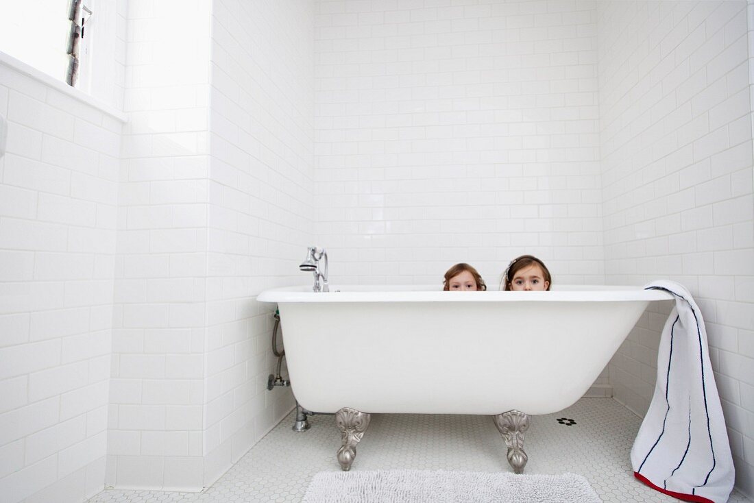 Portrait of two young girls peeking over bath