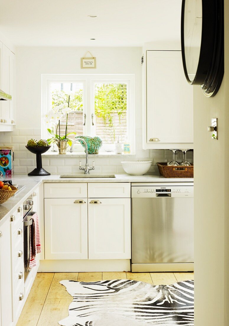 White fitted kitchen with Carrara marble worksurface and zebra-skin rug on wooden floor