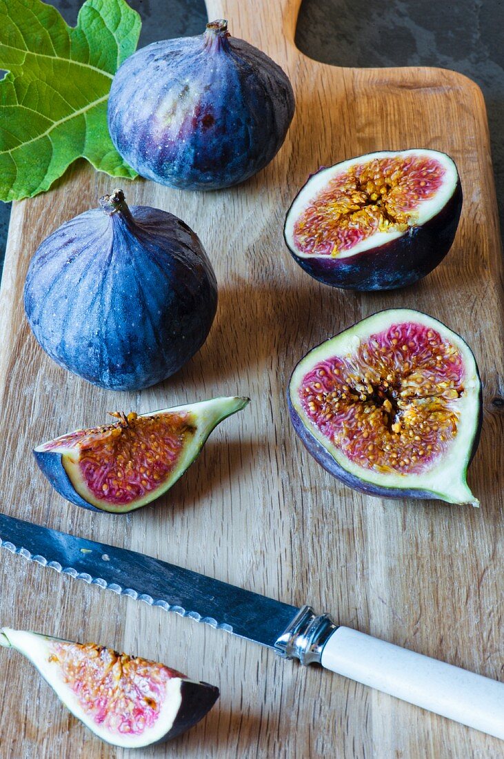 Cut fresh figs on a wooden board with a knife and fresh fig leaf.