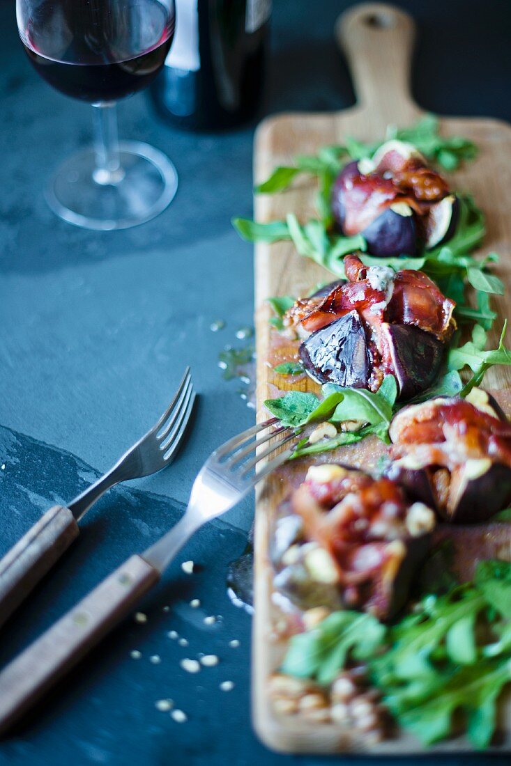 Gegrillte Feigen mit Blauschimmelkäse, Parmaschinken und Rucola auf Holzbrett