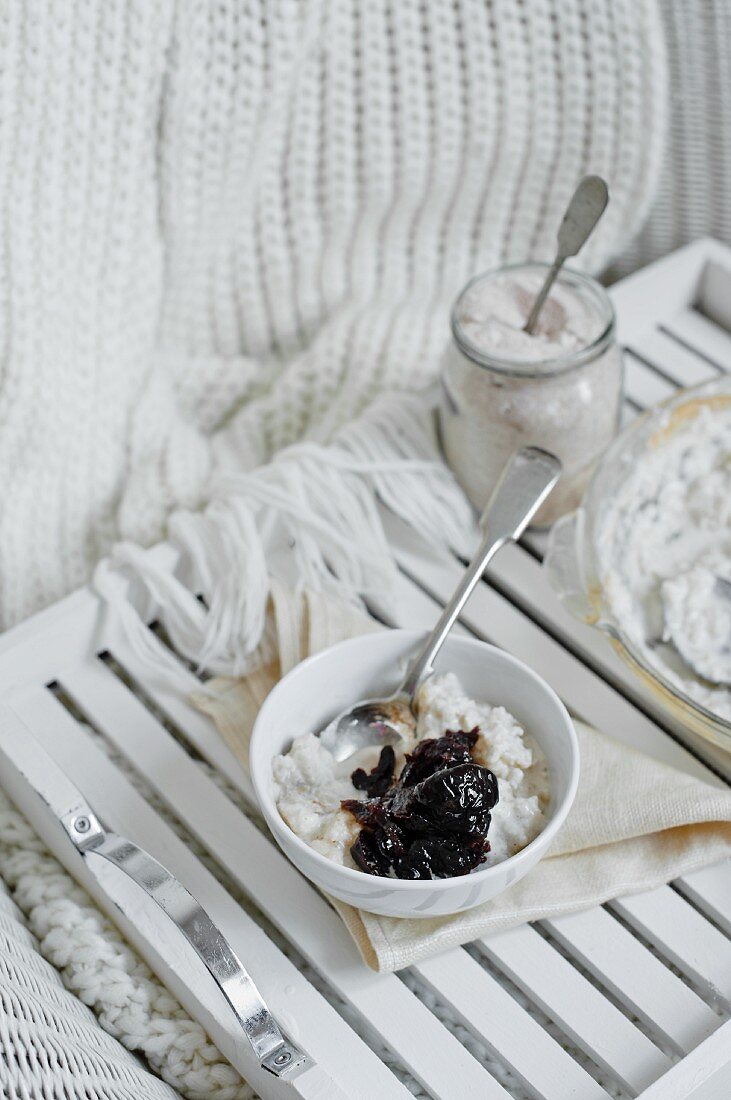 A bowl of rice puddding with prunes on a white tray.