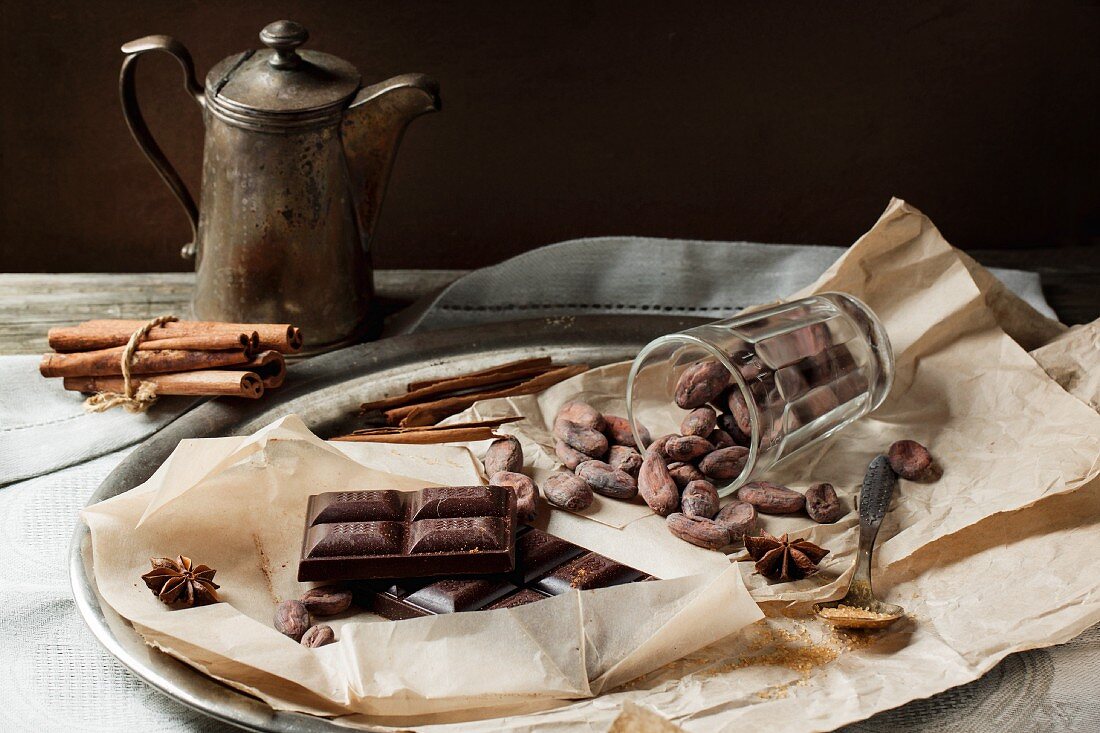 Bitterschokolade, Kakaobohnen und Gewürze vor Vintage-Kanne