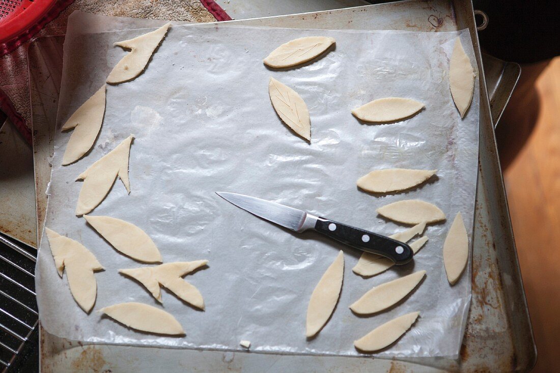 Ausgeschnittene Teigblätter zur Verzierung von Pies auf Backblech mit Messer