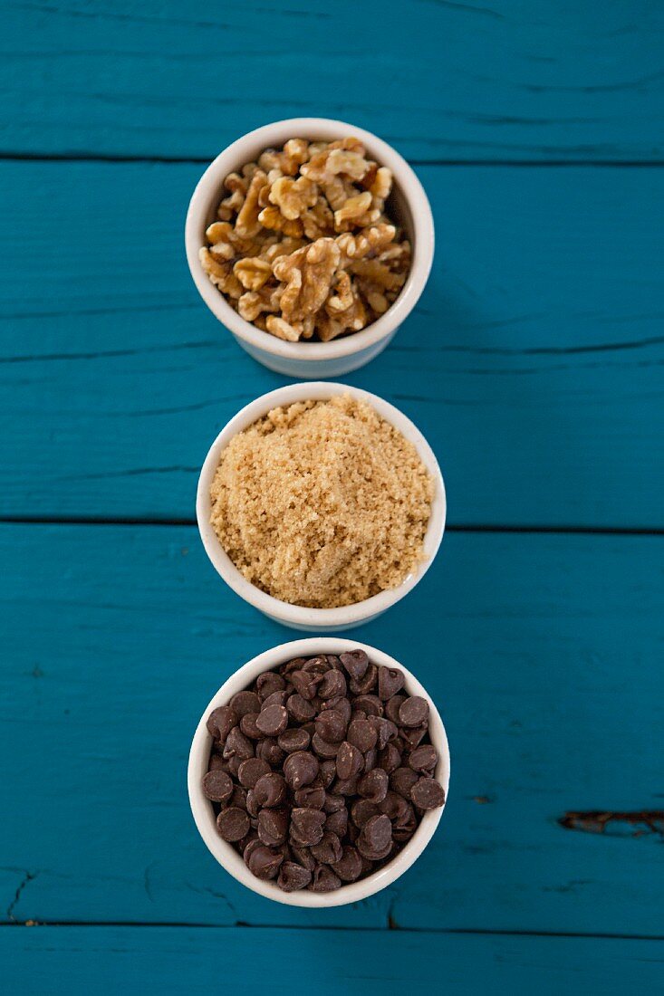 Small Cups Filled with Walnuts, Brown Sugar and Chocolate Chips on Blue Background