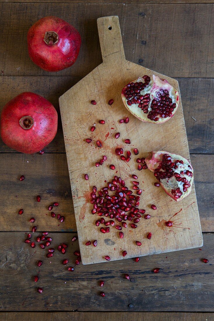 Sliced Pomegranate and Seeds on Cutting Board next to Whole Pomegranates