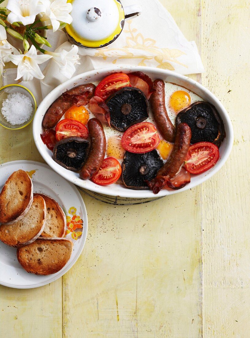 Frühstücksauflauf mit Würstchen, Spiegelei, Tomaten und Pilzen