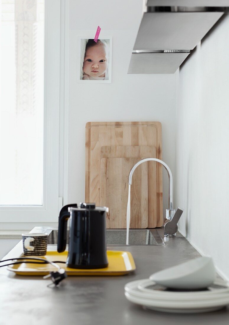 Kettle on yellow tray and sink in kitchen counter below baby photo