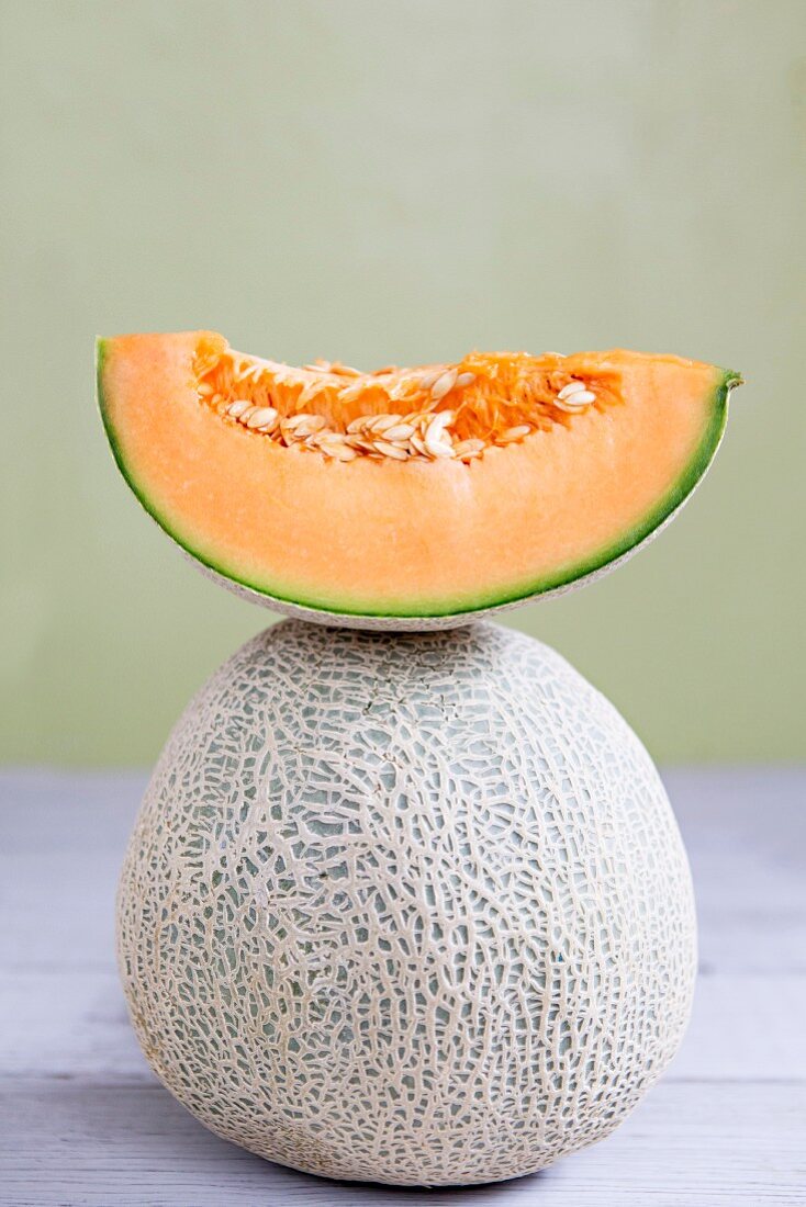 A slice of cantaloupe melon on top of a whole cantaloupe