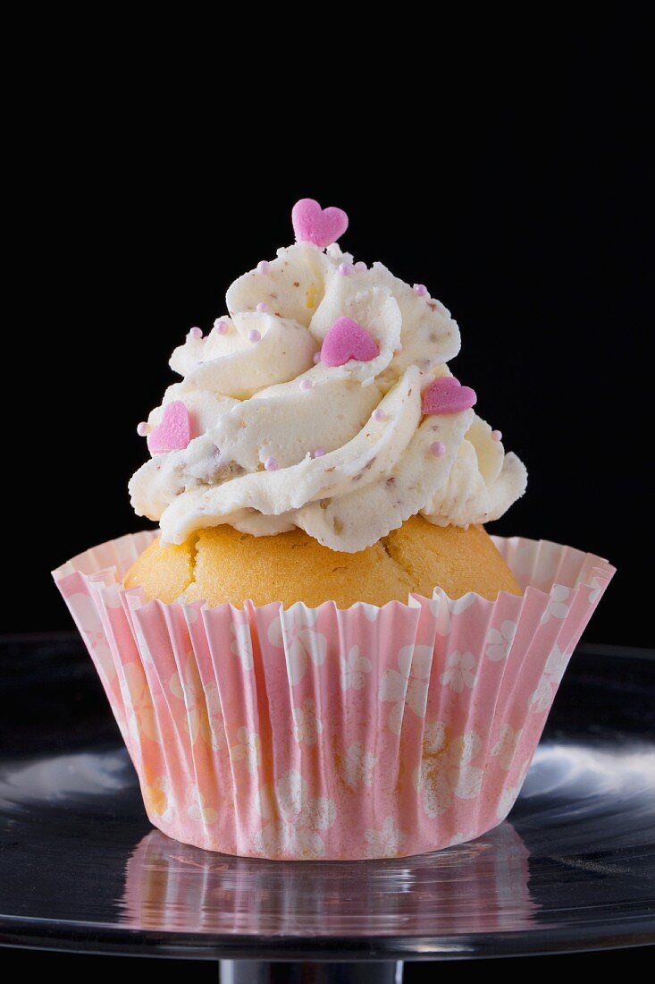 A cupcake decorated with buttercream and pink hearts