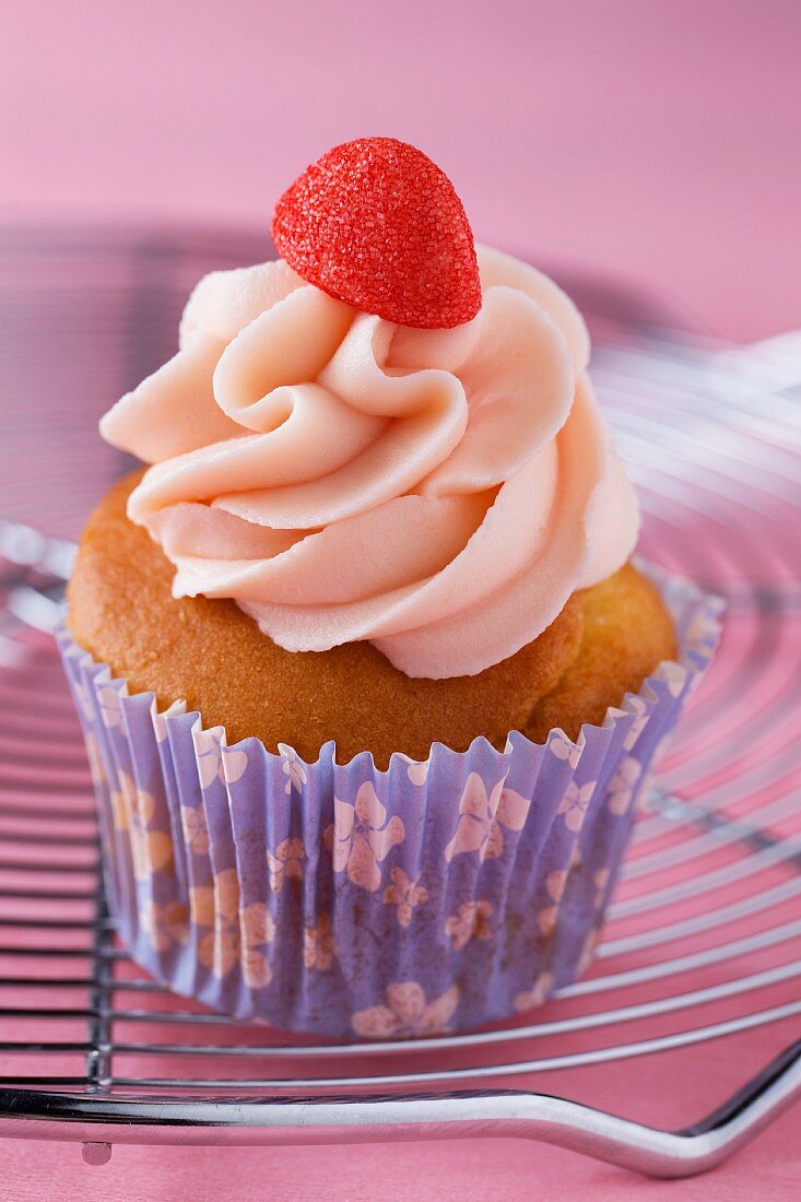 A cupcake decorated with strawberry cream and a strawberry bonbon