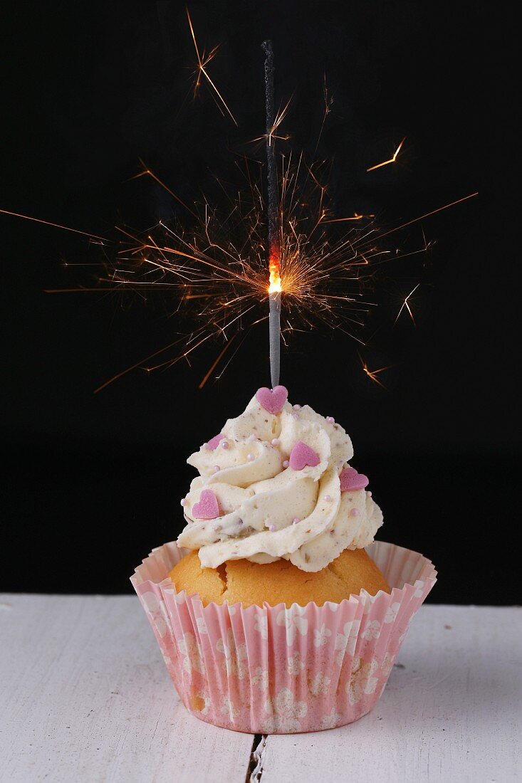 A cupcake decorated with pink hearts and a sparkler