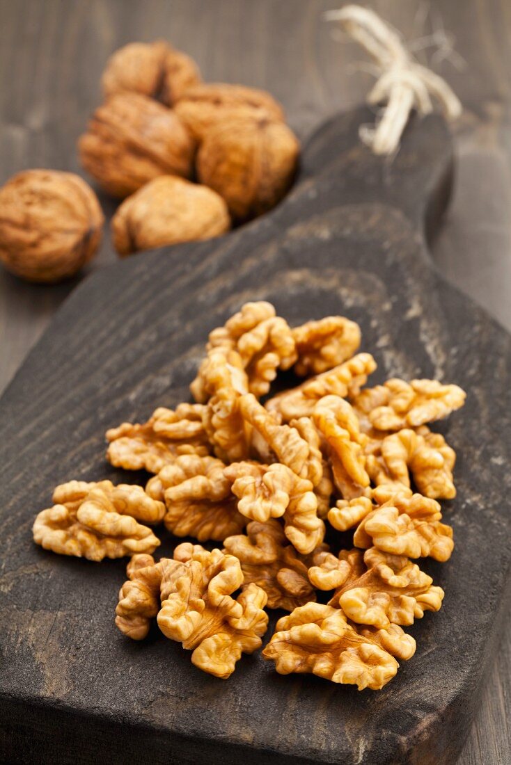 Walnuts on a wooden board next to whole walnuts in their shells
