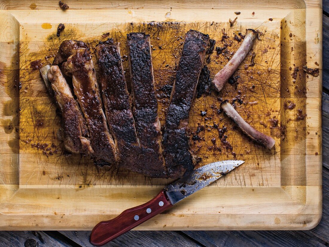 Gegrillte geschnittene Spareribs auf Schneidebrett mit Messer und Knochen (Draufsicht)