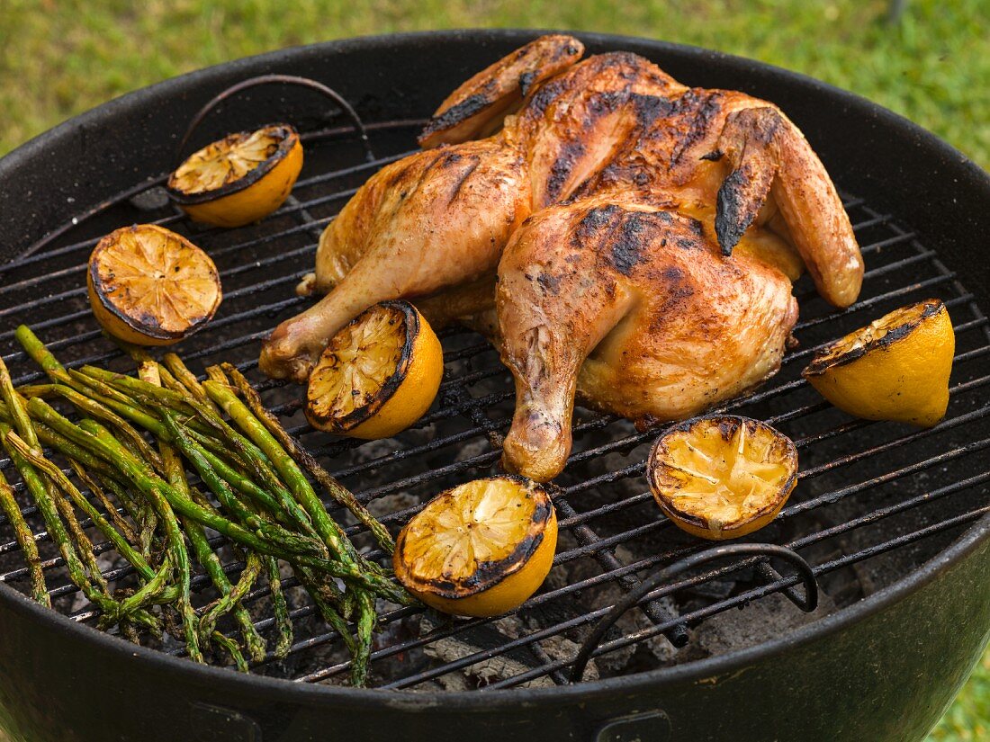 Whole chicken, split on the grill surrounded by lemons with asparagus