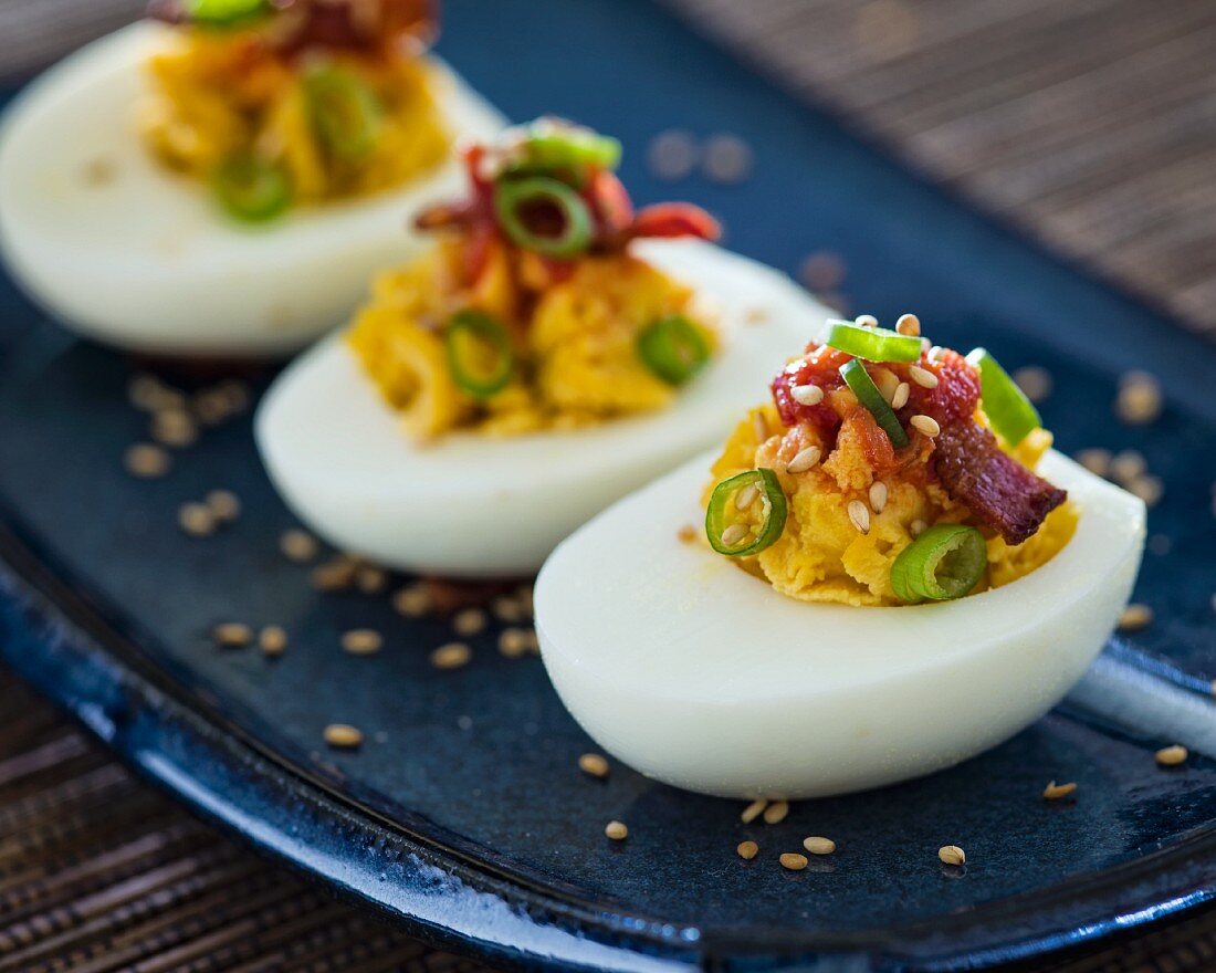 Three deviled egg halves with green onions and bacon sitting on a blue Asian-style plate