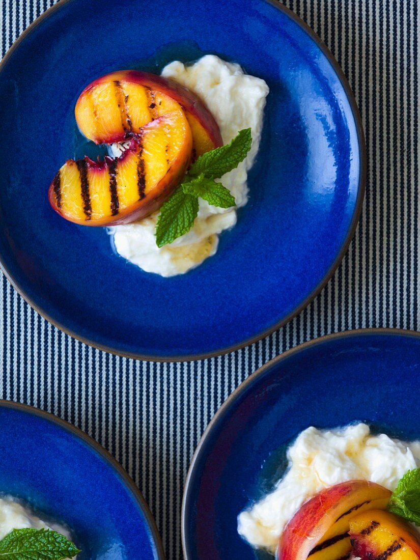 Grilled peaches on burrata drizzled with honey and garnished with mint leaves on cobalt blue plates