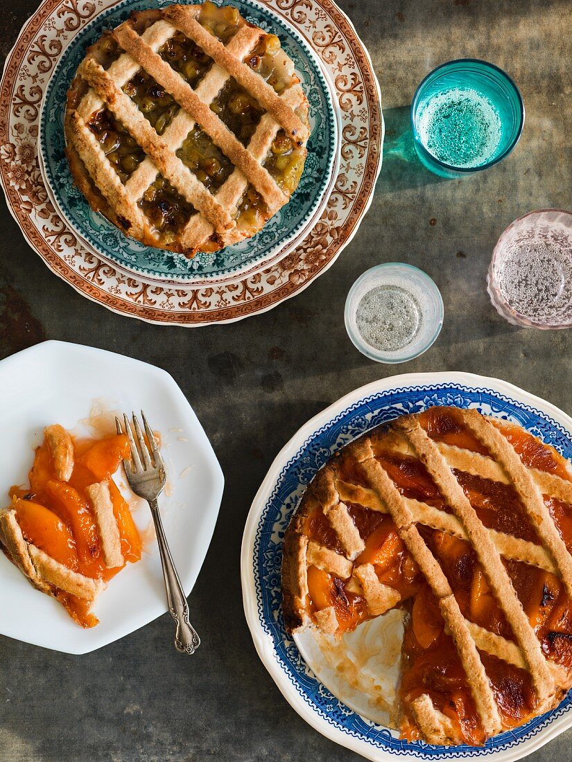 Gooseberry and peach pies with lattuce crust on vintage plates with colored glasses on an antiqued metal surface