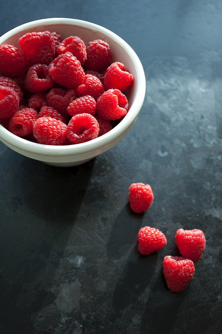 A bowl of fresh raspberries and four raspberries next to it
