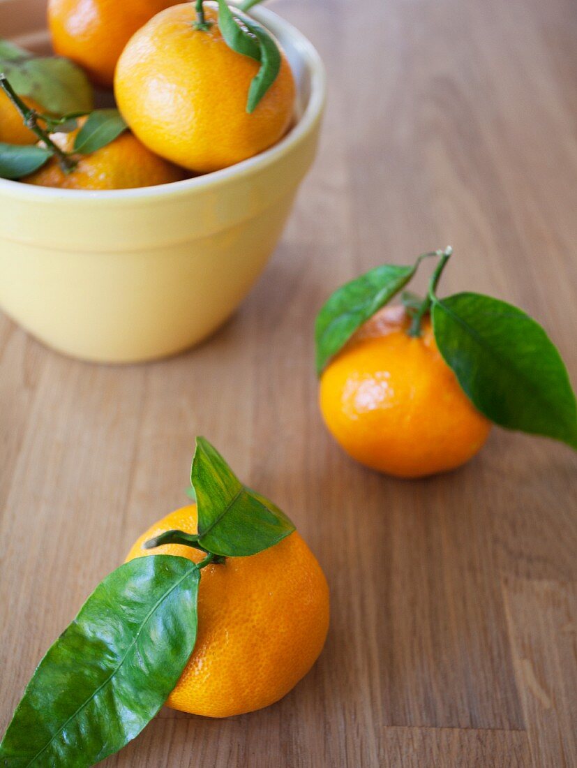 A bowl of clementines with leaves and two next to it