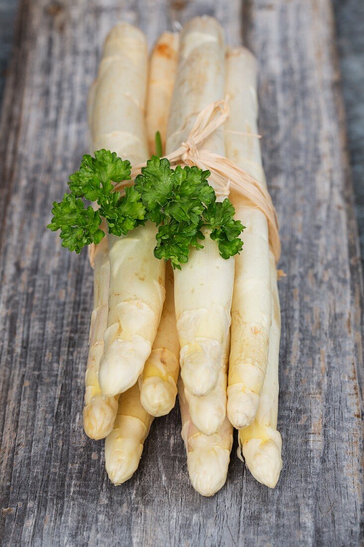 A bunch of white asparagus with parsley on a wooden surface