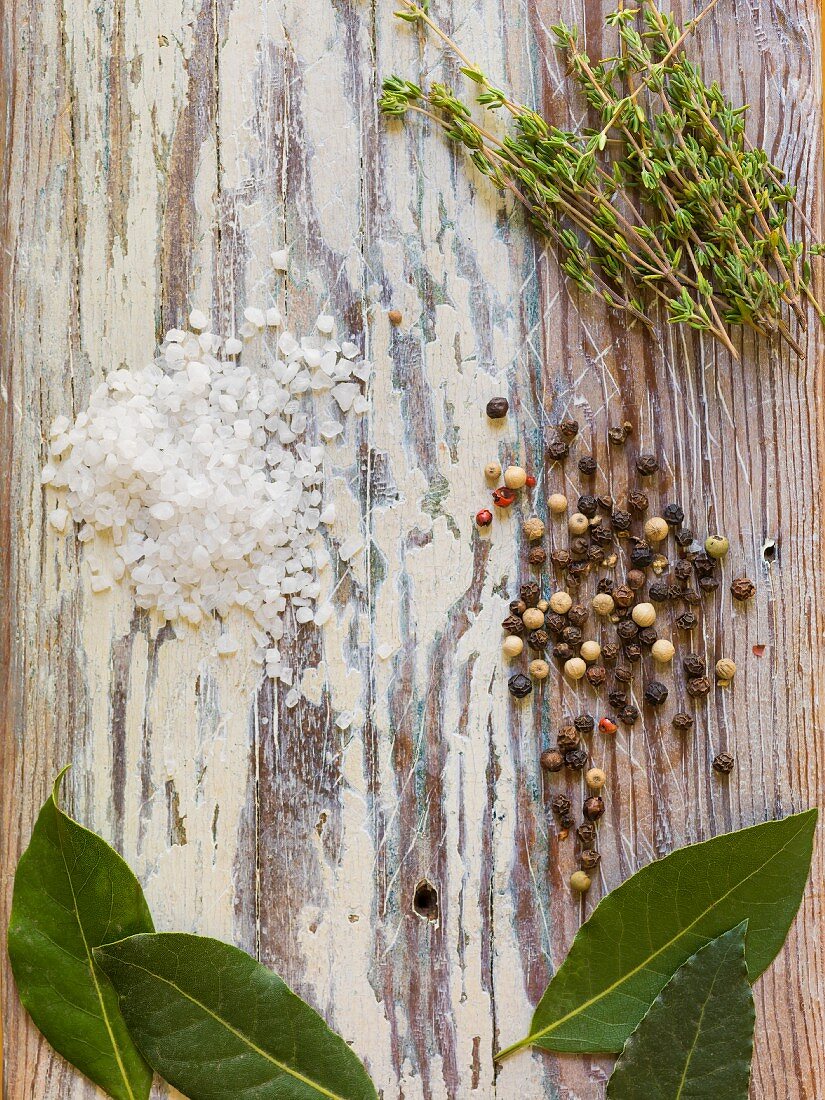 Thyme, bay leaves, peppercorns and coarse salt on a wooden surface