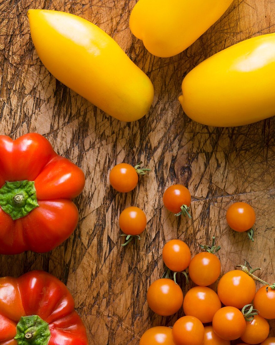 Yellow roma tomatoes, orange cherry tomatoes and heirloom peppers on an old chopping board