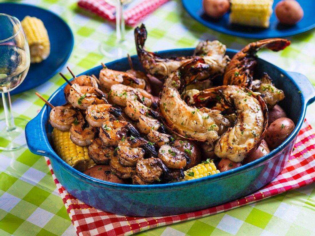 Grilled prawn kebabs and lobster tails on a bed of corn cobs and red potatoes