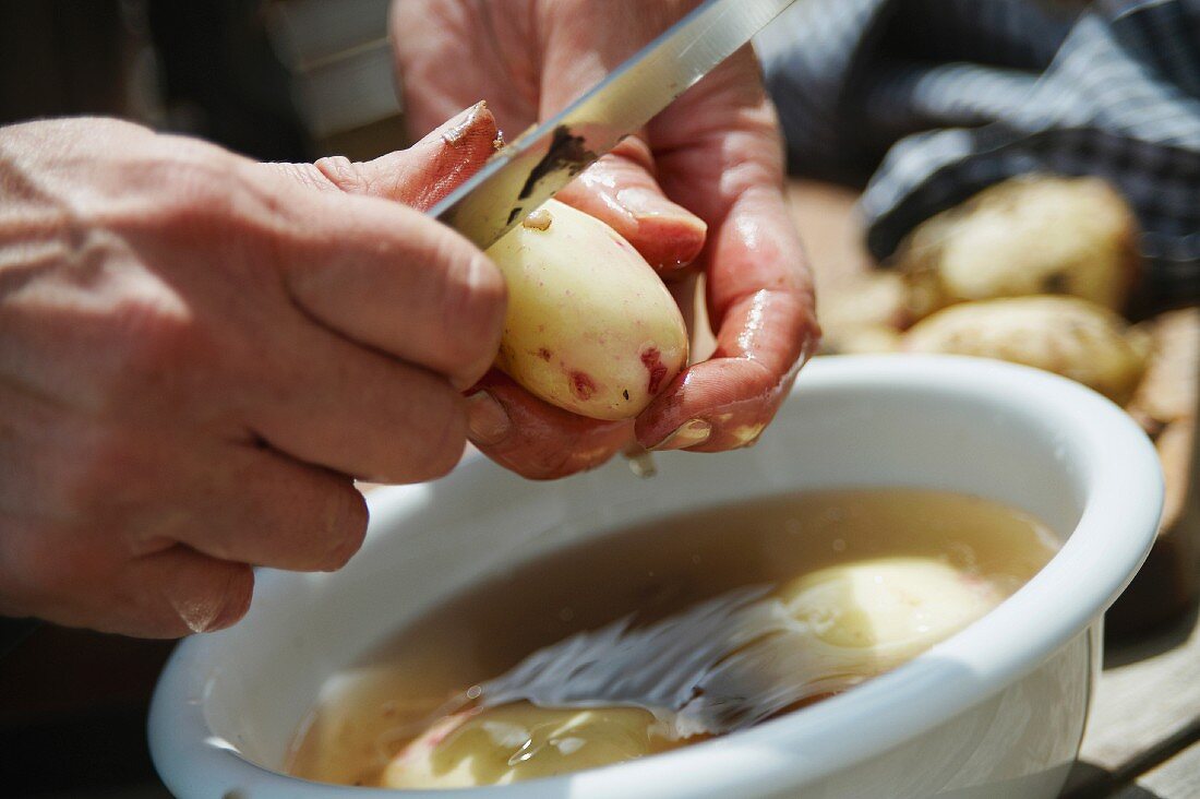 Kartoffeln über einer Wasserschüssel schälen