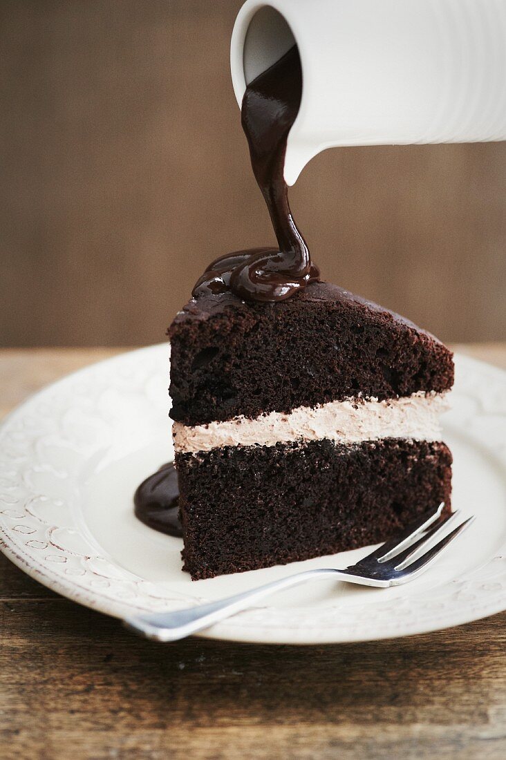 A slice of chocolate cake with a cream filling and chocolate sauce