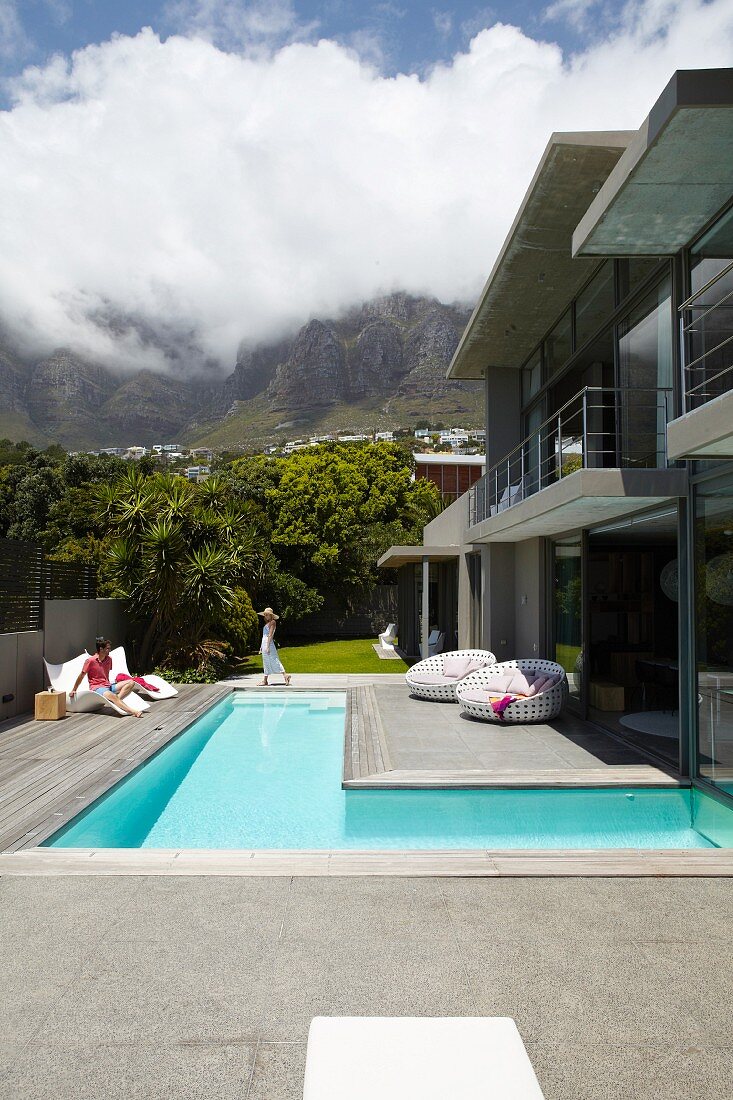 Luxury house with L-shaped floor, terrace and garden below white clouds in blue sky