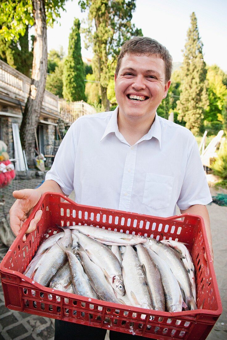 Mann hält rote Steige mit frischen Fischen