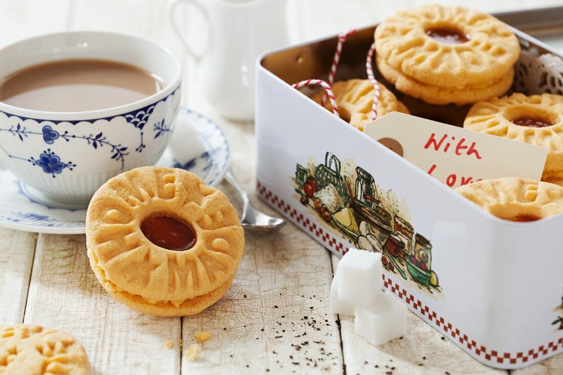 A tin of homemade jam and custard cream biscuits and a cup of tea